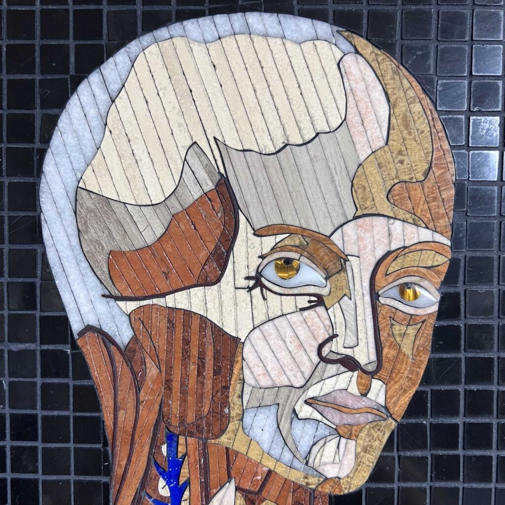 Detail of a marble mosaic face, the cranium partly stripped, the iris set in gold-toned stone, from Anatomy Set in Stone Table 26, 2021, by Rachael Que Vargas
