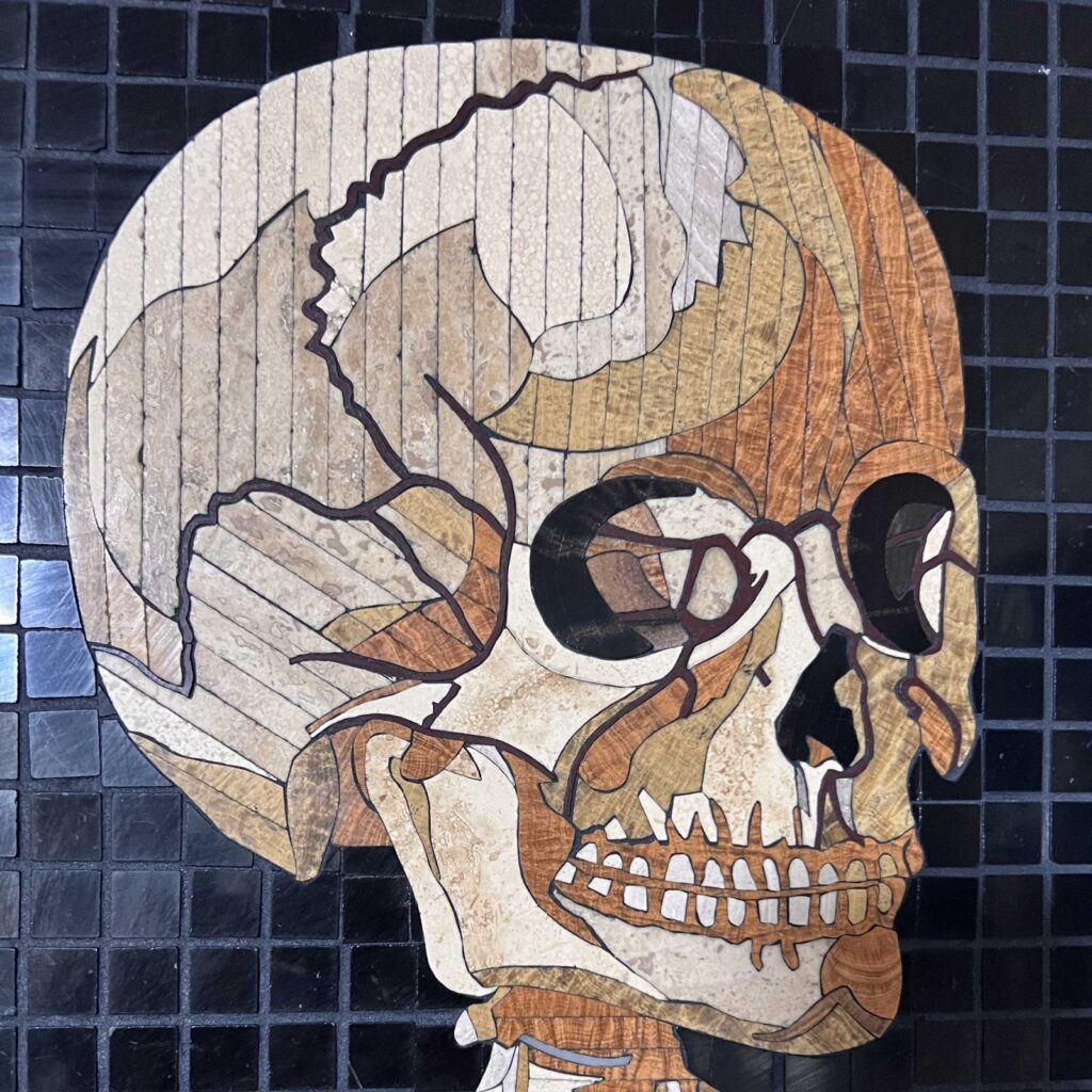 Detail of a marble mosaic skull showing the cranial suture cut as a single ribbon of stone, the eye socket, and the teeth, from Anatomy Set in Stone Table 43, 2020, by Rachael Que Vargas